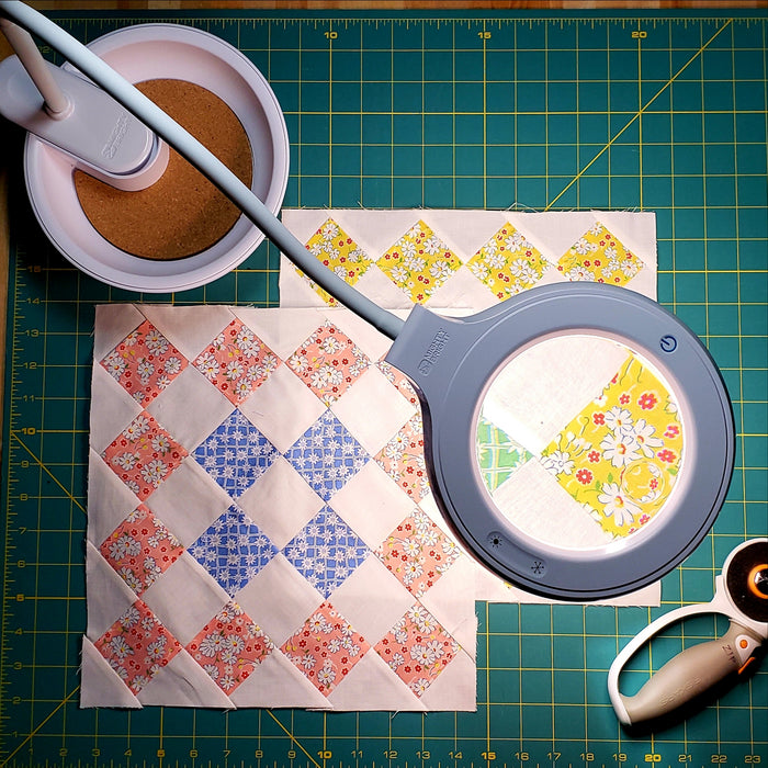 The Magnifier Task Lamp with Pincushion base with quilting squares and quilting supplies.